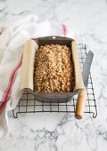 Banana bread in a loaf tin on a wire rack