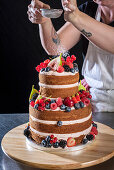 Sprinkling icing sugar on a wedding cake with almond layers, raspberry buttercream, raspberry filling and fruit