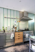 Island counter with stainless steel and wooden fronts below frosted glass wall