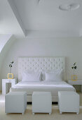 Double bed with white headboard and white cubic pouffes in bedroom