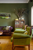 Green armchairs, half-height cabinet and vintage leather sofa in living room with green walls