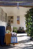 Blanket on blue armchair, wooden barrel, green chair and trunk on roofed veranda