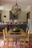 Dining table and upholstered chairs below pendant lamp with glass lampshade in open-plan kitchen