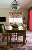 Dining table and upholstered chairs below pendant lamp with glass lampshade in open-plan interior