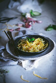 Appetizing pasta with vegetables basil in black bowl on served table