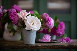 Pinkfarbene und weiße Rosen im Metallgefäßen auf Holztisch