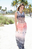 A brunette woman on the beach wearing a light summer dress with an ethnic pattern