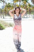 A brunette woman on the beach wearing a light summer dress with an ethnic pattern