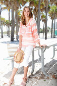 A brunette woman on the beach wearing a batik tunic and white trousers