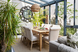 Upholstered chairs around wooden table in conservatory with tropical character