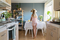 Girl wearing pyjamas setting breakfast table in open-plan kitchen-dining room