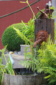 Pflanzkübel mit Farn am Wasserspeier und Dekofiguren im Garten