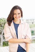 A young brunette woman wearing a blue t-shirt with a pale pink shirt blouse