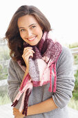 A young brunette woman wearing a grey woollen jumper and a thick scarf