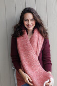 A young brunette woman wearing a wine-red cardigan with a salmon pink woollen shawl