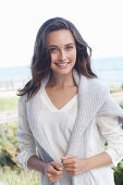 A young brunette woman wearing wearing a white tunic with a woollen jumper over her shoulders