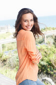 A young brunette woman wearing a salmon-pink tunic blouse