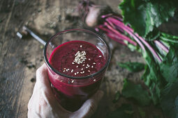 Hand hält Rote-Bete-Smoothie mit Sesam auf Holztisch