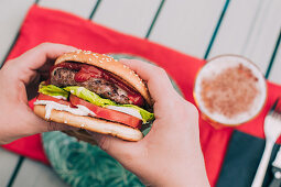 Hands holding a delicious homemade cheeseburger with lettuce, tomato and sauces