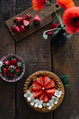 Mini-Erdbeertarte auf Holztisch daneben Mohnblume in Vase (Aufsicht)