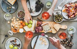 Charcuterie and cheese board, rose wine, nuts, olives and peoples hands with snacks and wine