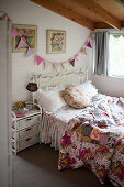 Old bed with colourful, vintage-style bed linen and rattan bedside table below bunting on wall