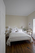 Blick auf weißes Doppelbett mit weißer Tagesdecke im Schlafzimmer mit dunklem Holzdielenboden