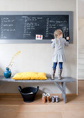 Girl standing on grey wooden bench drawing on chalkboard
