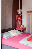 Matratze mit pinkfarbenem Spanntuch, daneben farblich passender Hocker mit Spiegel im Schlafzimmer