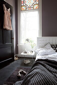 Bett mit schwarz-weißer Bettwäsche, Damenwäsche an schwarzer Tür im Schlafzimmer mit dunkler Wand