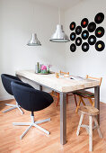 Arrangement of vinyl records on wall above dining table with various chairs