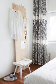 Weiße Bluse an Holzpaneel, Hocker und schwarz-weißer Vorhang im Schlafzimmer
