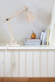 Reading lamp, books, and a pear on a shelf in the sloping ceiling