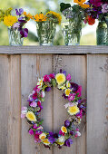 Blumenkranz und Sträußchen in Wassergläsern an einer Bretterwand