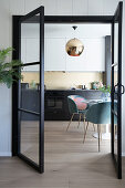 A view through an open glass door into a kitchen with a round table and shell chairs