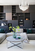 A dark living room wall with upholstered furniture a round coffee table and a chandelier