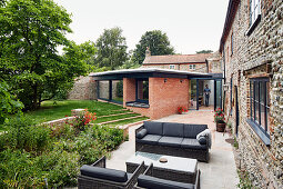 Garden view of extension and existing brick and flint farmhouse with patio furniture