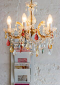 A colourful chandelier in front of a white wall with magazine rack