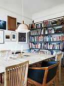 Different chairs at the dining table in front of the bookshelf and a salon style picture wall