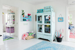 Light blue display cabinet with books, seat cushions, and a little suitcase on top