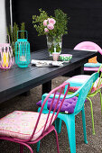 Colourful chairs with cushions around a black wooden table with lanterns and a bouquet of roses