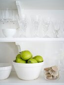 Green pears in a bowl on a kitchen shelf with glasses