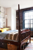 An antique double bed with a wooden frame, a built-in wardrobe and a window in a bedroom with exposed brickwork