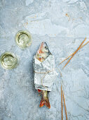 Wineglasses and raw fish wrapped in newspaper