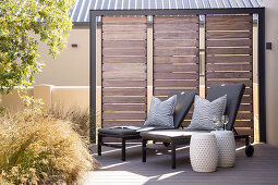 Two loungers and ceramic stools on sunny terrace with screen