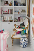 Cushions on antique armchair and chine pot on floor in front of white bookcase