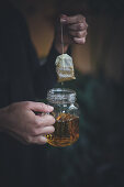 A woman holding a dripping teabag and a hot herbal tea