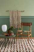 Macrame wall hanging above chair and low round table on patterned carpet