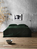 Double bed with green bedspread and floor lamp against gray wall
