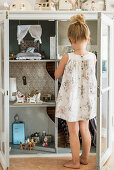 Girl standing in front of dolls' house in converted display case